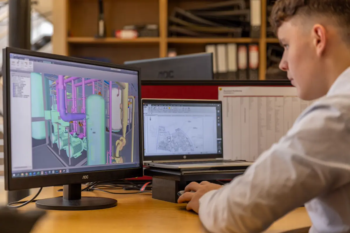 Engineer working on a 3D CAD model and a 2D plan across dual monitors